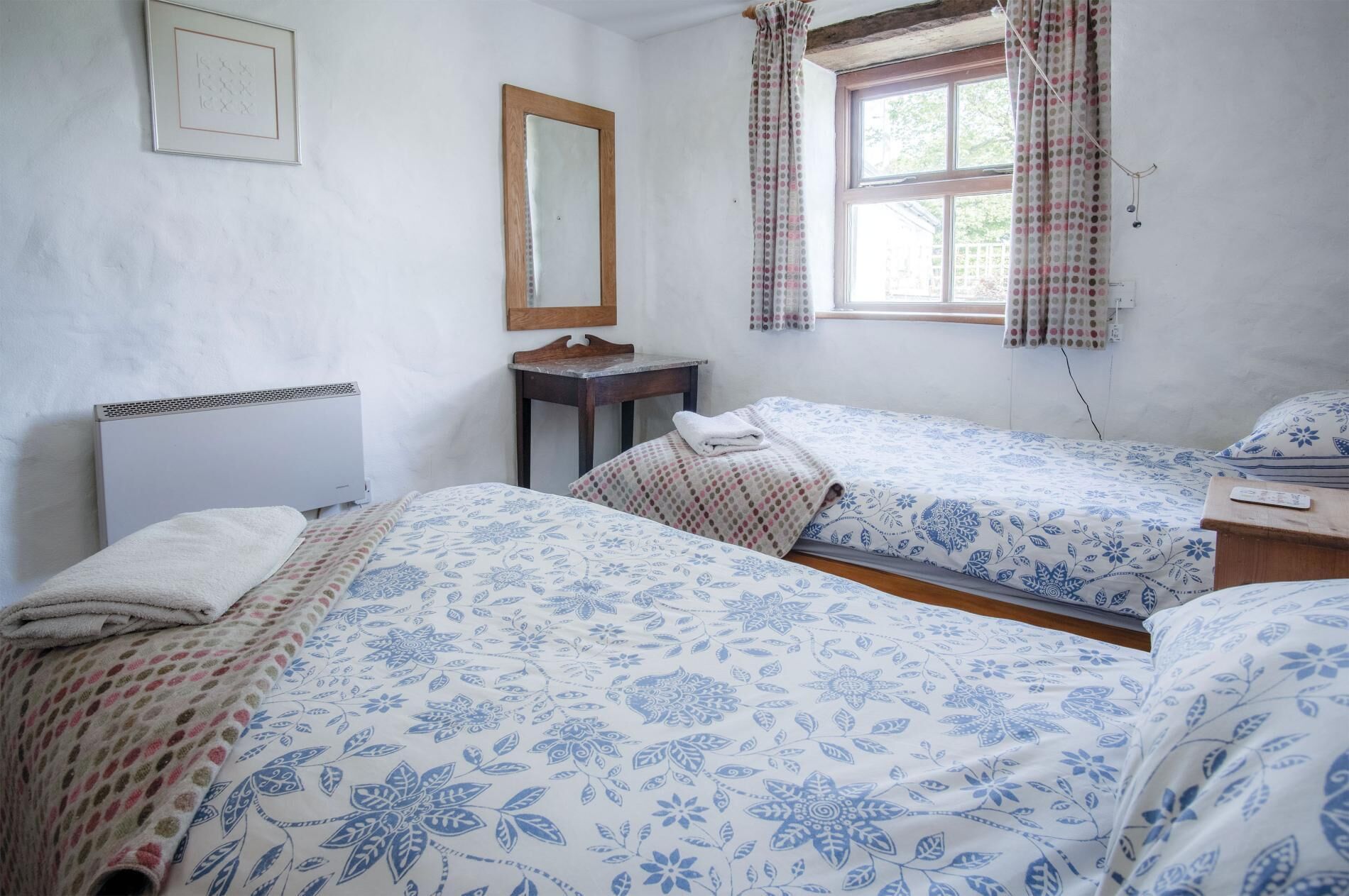 Een slaapkamer met twee bedden, een houten hoofdbord, een kleine tafel, een spiegel en een raam met gordijnen.