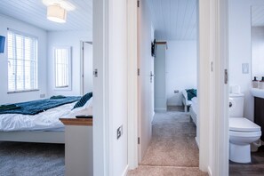 A hotel room with a bed, a desk, a bathroom with a toilet and sink, and a hallway leading to another room. - Swallow Lodge - 3 Bedroom Lodge - Wisemans Bridge (Narberth)