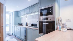 A modern kitchen with grey cabinets, a wooden countertop, a built-in oven, and a dishwasher. - 25 Captains Walk - 1 Bedroom Apartment - Saundersfoot (Saundersfoot)