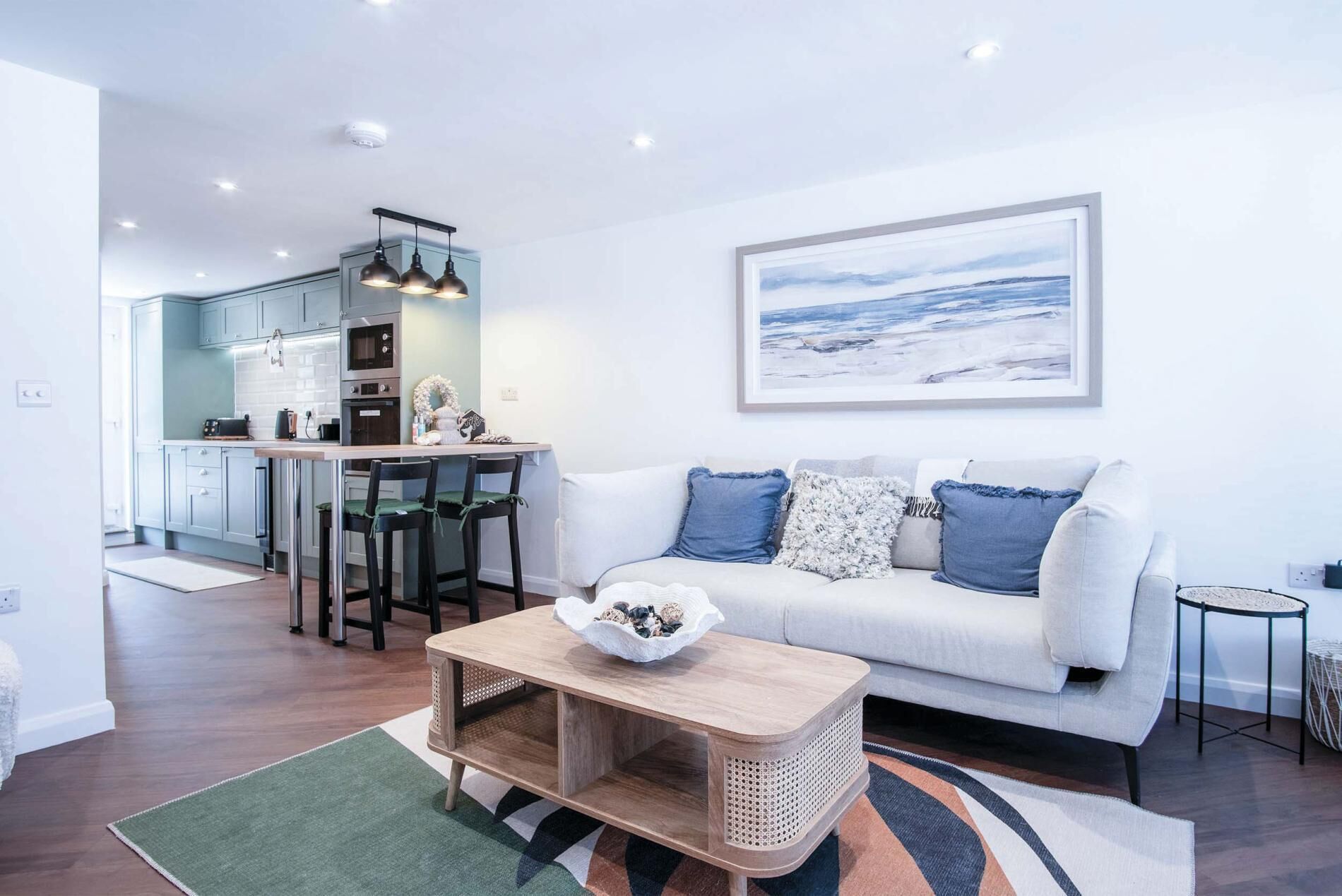 A modern living room with a white sofa, a coffee table, and a kitchen in the background.