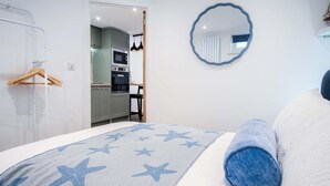 A bedroom with a bed, a round mirror, and a kitchenette in the background. - 25 Captains Walk - 1 Bedroom Apartment - Saundersfoot (Saundersfoot)