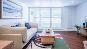 A modern living room with a beige sofa, a rattan coffee table, and a colorful rug. - 25 Captains Walk - 1 Bedroom Apartment - Saundersfoot (Saundersfoot)