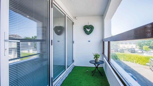 A balcony with a green artificial turf, a small round table with a potted plant, and a heart-shaped decoration on the wall. - 25 Captains Walk - 1 Bedroom Apartment - Saundersfoot (Saundersfoot)