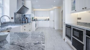 Een moderne keuken met granieten aanrechtbladen, witte kastjes en roestvrijstalen apparatuur.