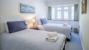 Een hotelkamer met twee bedden, een schilderij aan de muur, een raam met gordijnen en een lamp op een nachtkastje.
