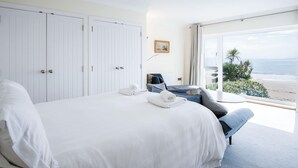 Een hotelkamer met een groot bed, een zithoek met uitzicht op het strand en een witte inloopkast.