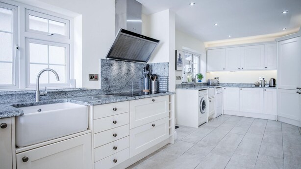Een moderne keuken met witte kasten, granieten werkbladen, een inbouwoven en een roestvrijstalen afzuigkap.