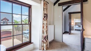 A room with a large window, a radiator, a door leading to another room, and a bed with a nightstand.