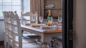 A dining table set for four with white chairs, a bottle of champagne, and empty wine glasses.