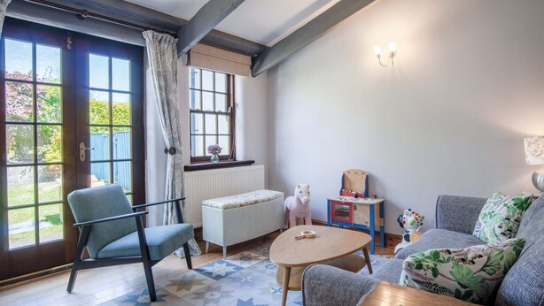 A cozy living room with a blue chair, a round wooden table, a sofa with floral cushions, and a white horse toy.