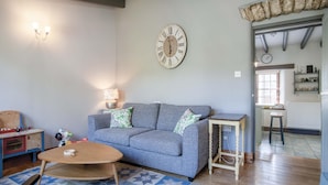 A living room with a grey sofa, a wooden coffee table, a patterned rug, and a wall clock.