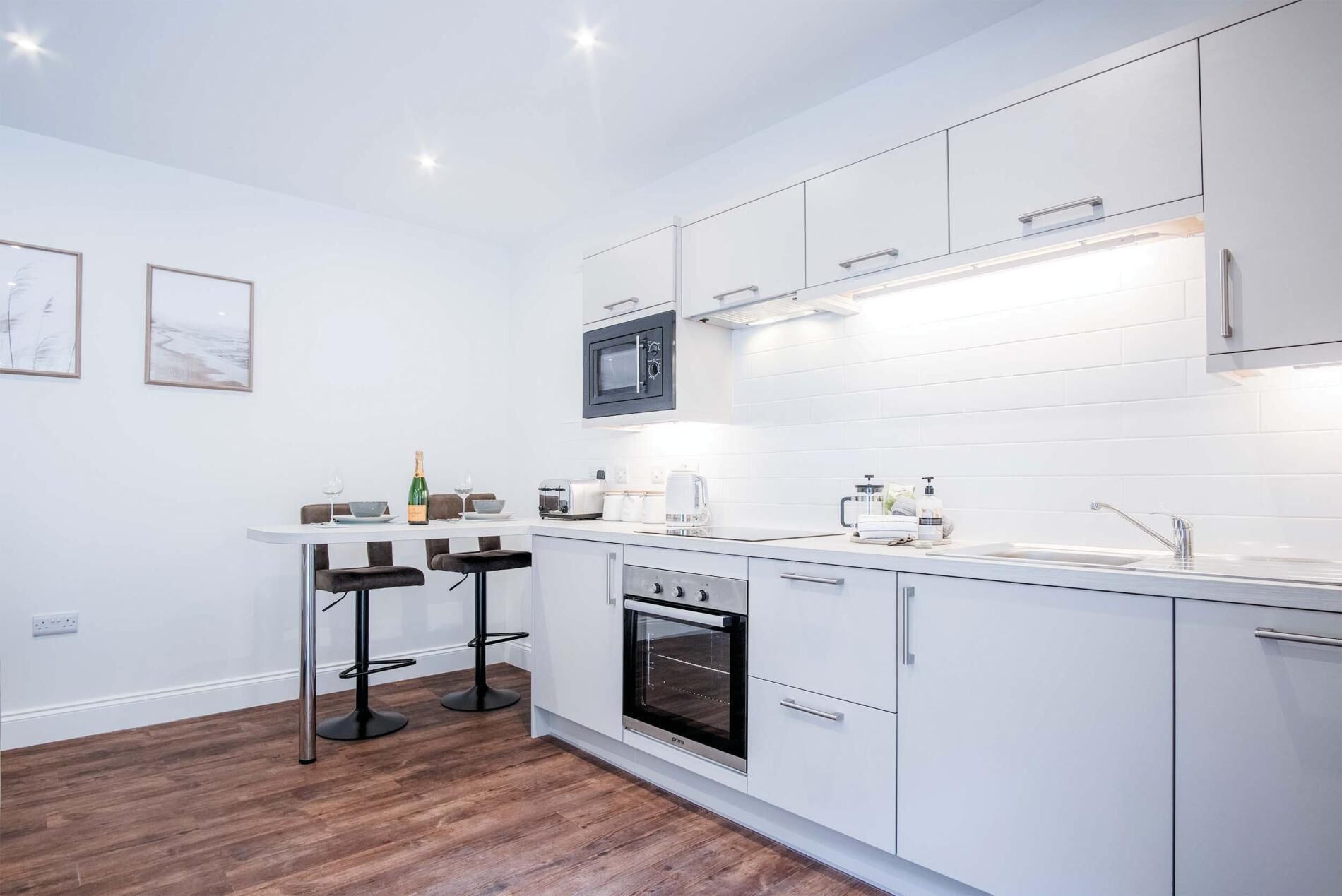 A modern kitchen with white cabinets, a built-in microwave, a toaster, and a wine bottle on the counter.
