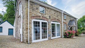 A stone building with large arched windows and a gravel driveway. - The Carthouse - 1 Bedroom Cottage - Princes Gate (Narberth)