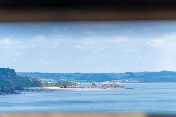 A coastal landscape with a prominent rock formation in the distance, a sandy beach, and rolling hills.