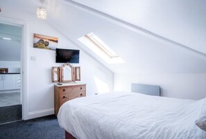 A bedroom with a bed, a dresser, a TV mounted on the wall, and a skylight. - Rooftops - 1 Bedroom Apartment - Tenby (Tenby)