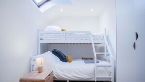 A bunk bed room with a skylight, a bedside table with a lamp, and a small wooden dresser. - The Cottage - 2 Bedroom Cottage - Tenby (Tenby)