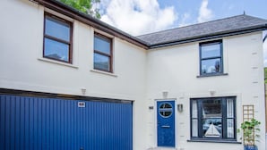A two-story building with a blue garage door, a blue front door, and a small window with a sailboat decoration. - The Cottage - 2 Bedroom Cottage - Tenby (Tenby)