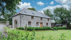 Une maison en pierre avec un toit en pente, de nombreuses fenêtres et une pelouse bien entretenue.