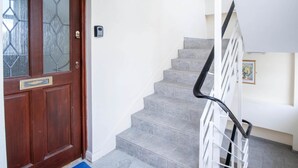 A wooden door with a glass panel, a white wall, and a staircase with grey tiles and a black handrail. - Harbour Hideaway - 1 Bedroom Apartment - Saundersfoot (Saundersfoot)