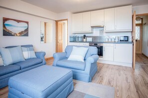 A modern living room with a sofa set and a kitchen area with white cabinets and appliances. - Harbour Hideaway - 1 Bedroom Apartment - Saundersfoot (Saundersfoot)