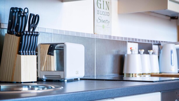 A kitchen with a toaster, a knife block, and a sign that reads "GIN IS LIQUID Sanity". - Harbour Hideaway - 1 Bedroom Apartment - Saundersfoot (Saundersfoot)