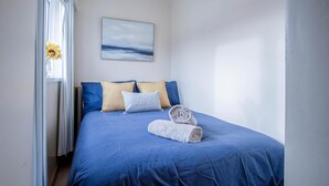 A neatly made bed with a blue bedspread, two pillows, and a rolled towel. - Harbour Hideaway - 1 Bedroom Apartment - Saundersfoot (Saundersfoot)