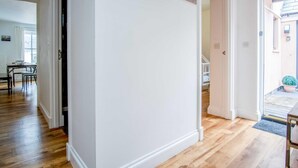 A hallway with wooden flooring, white walls, and a door leading to a room with a bed and a window. - Kensington Apartment - 2 Bedroom - Saundersfoot (Saundersfoot)