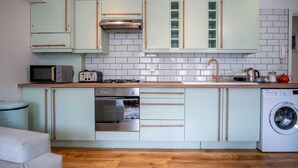 A compact kitchen with light blue cabinets, a stainless steel range, a microwave, a toaster, a sink, and a washing machine. - Kensington Apartment - 2 Bedroom - Saundersfoot (Saundersfoot)