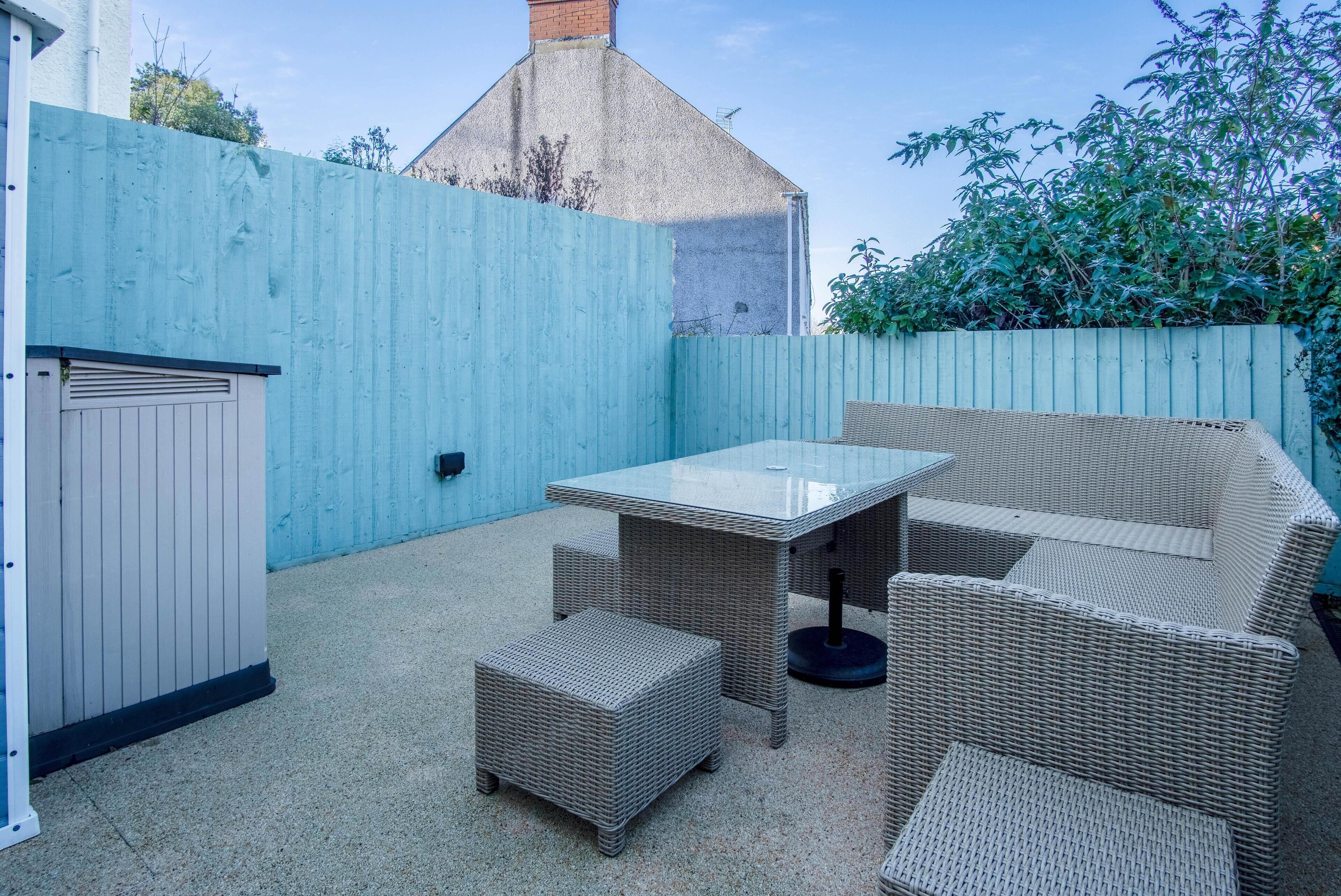 A patio area with a table and wicker furniture, a white door, and a blue fence.