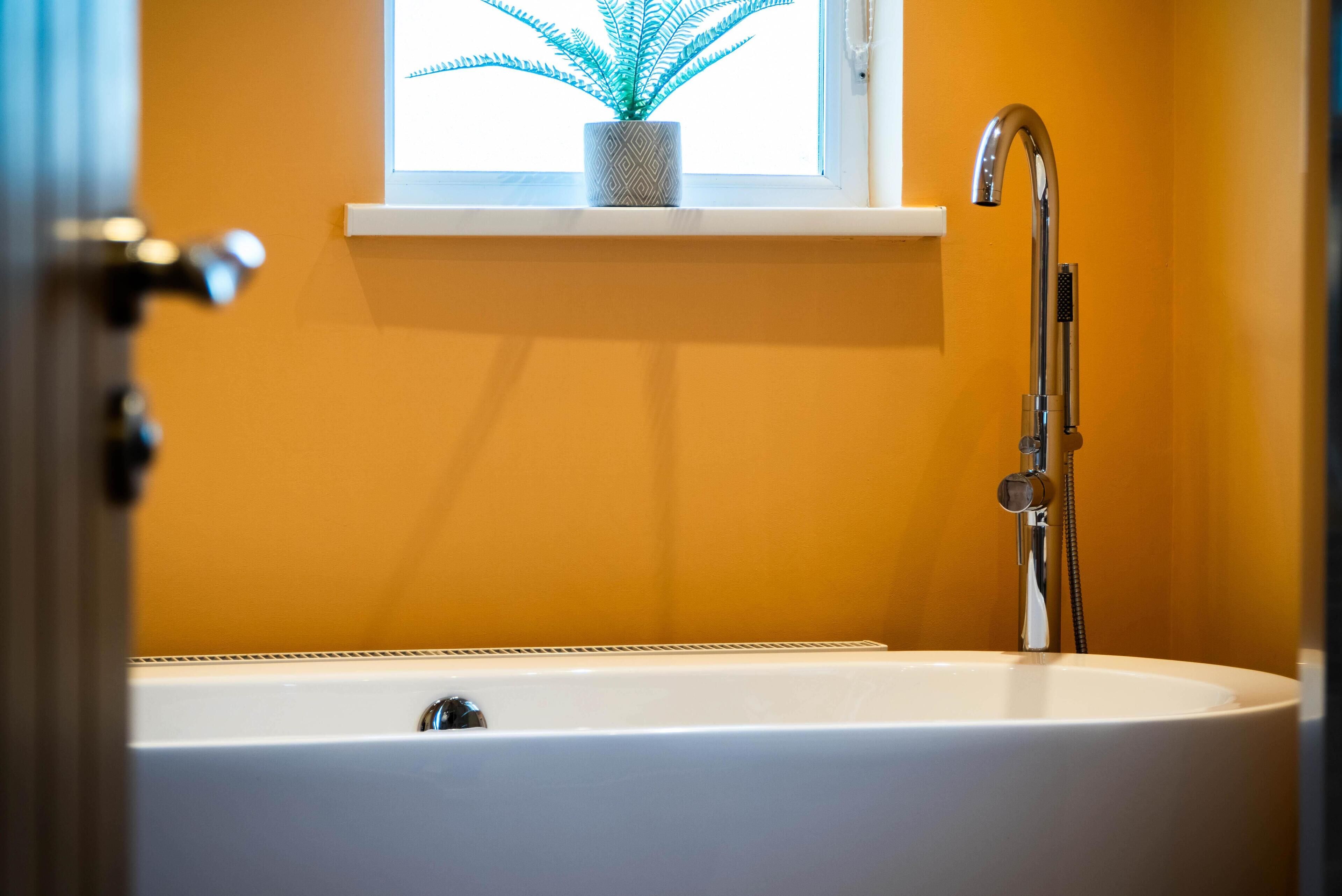 A bathroom with a white bathtub, a modern faucet, and a window with a plant.