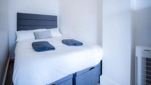 A neatly made bed with white linens and two folded blue blankets.