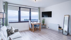A modern living room with a large window, a flat-screen TV, a dining table, and a sofa.
