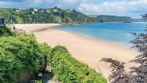 A beach with a clear view of the sea, surrounded by lush greenery and a few buildings in the background. - 5 Belle Vue Court - 2 Bedroom Apartment - Tenby (Tenby)