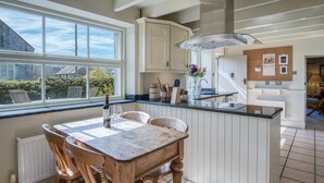 A kitchen with a wooden dining table, white cabinetry, and a large window. - Fern Cottage - 2 Bedroom Cottage - St Florence (Tenby)