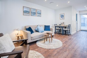 A modern living room with a sofa, two side tables, a coffee table, and a dining area with a table and chairs.