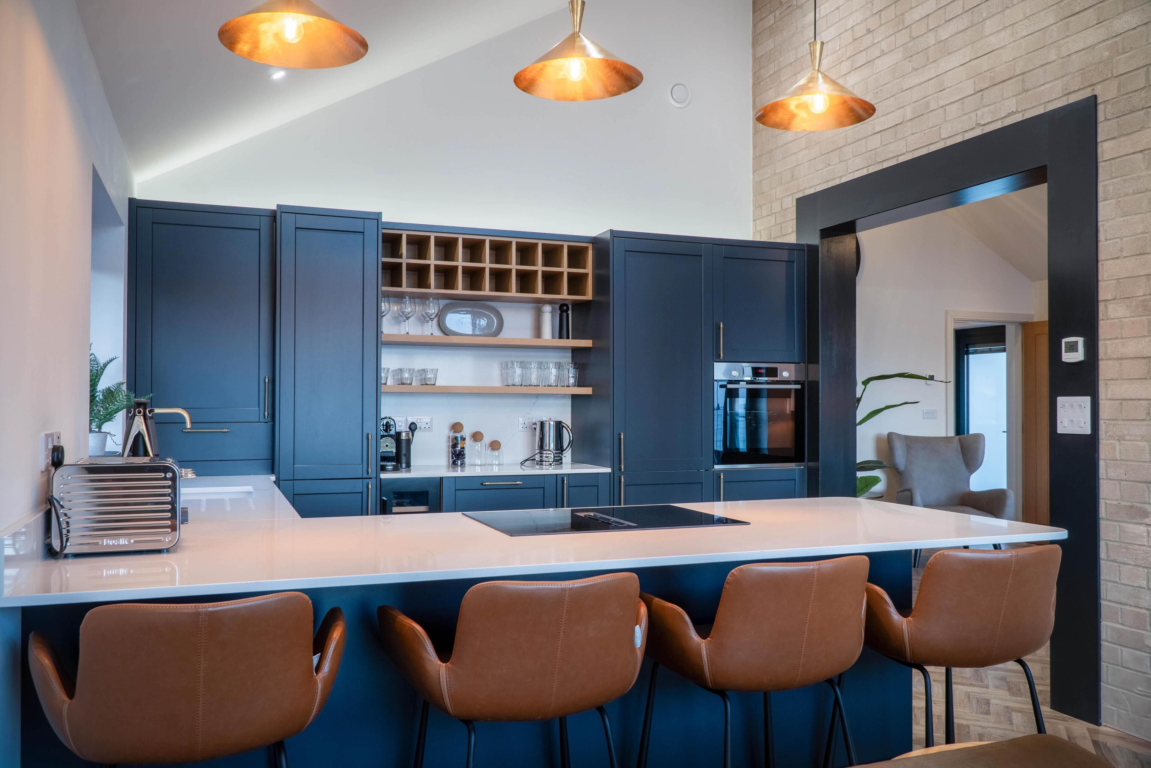 Una cocina moderna con armarios azul oscuro, una isla central con taburetes altos e iluminación colgante.