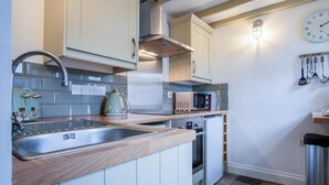 A kitchen with a sink, stove, microwave, and kettle.
