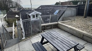 A rooftop patio with a wooden table and benches, surrounded by a metal fence.