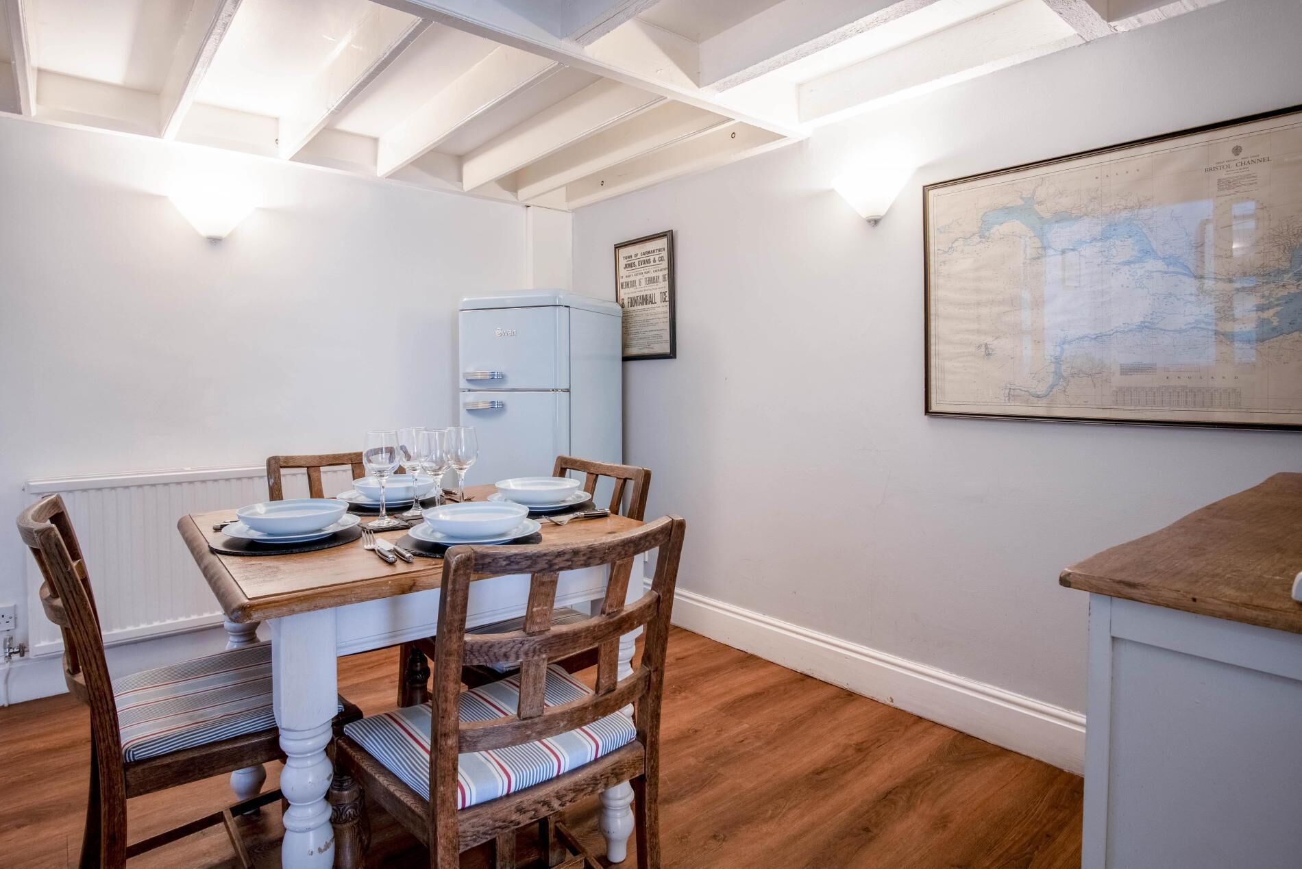 A dining area with a wooden table set for four, a vintage blue refrigerator, and a map on the wall.