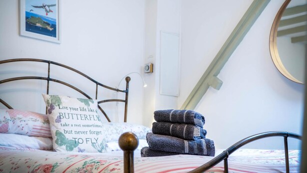 A bedroom with a bed, pillows, a framed picture of Caldey Island, and a stack of towels.