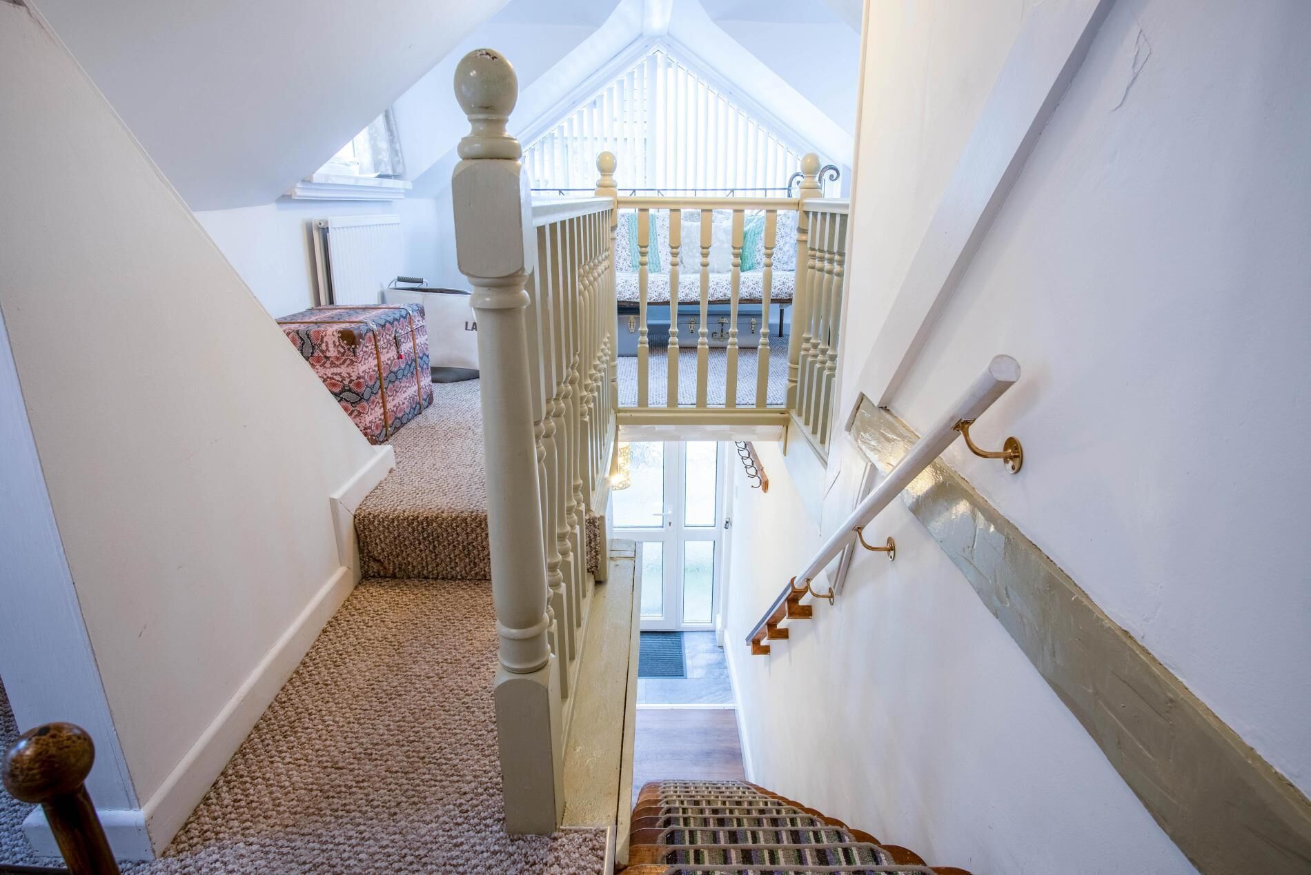 Eine Treppe mit Holzhandlauf, Teppichstufen und Blick auf einen Balkon mit Geländer.