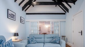 A living room with a blue sofa, two side tables, and a wooden coffee table. There are framed pictures on the wall and a white door on the right.