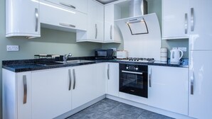 A modern kitchen with white cabinets, a black stove, and a Bosch oven. - Ridgeway Hideaway - 1 Bedroom Holiday Home - Manorbier (Tenby)