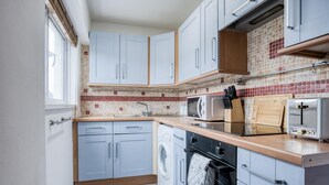 A compact kitchen with light blue cabinets, a tiled backsplash, a washing machine, a microwave, and a toaster.