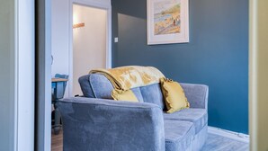 A room with a blue wall, a framed picture, and a blue sofa with a yellow pillow.
