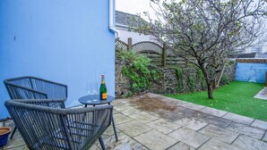 Een terras met twee rieten stoelen en een kleine tafel, een fles champagne, en een vloer van stenen tegels.