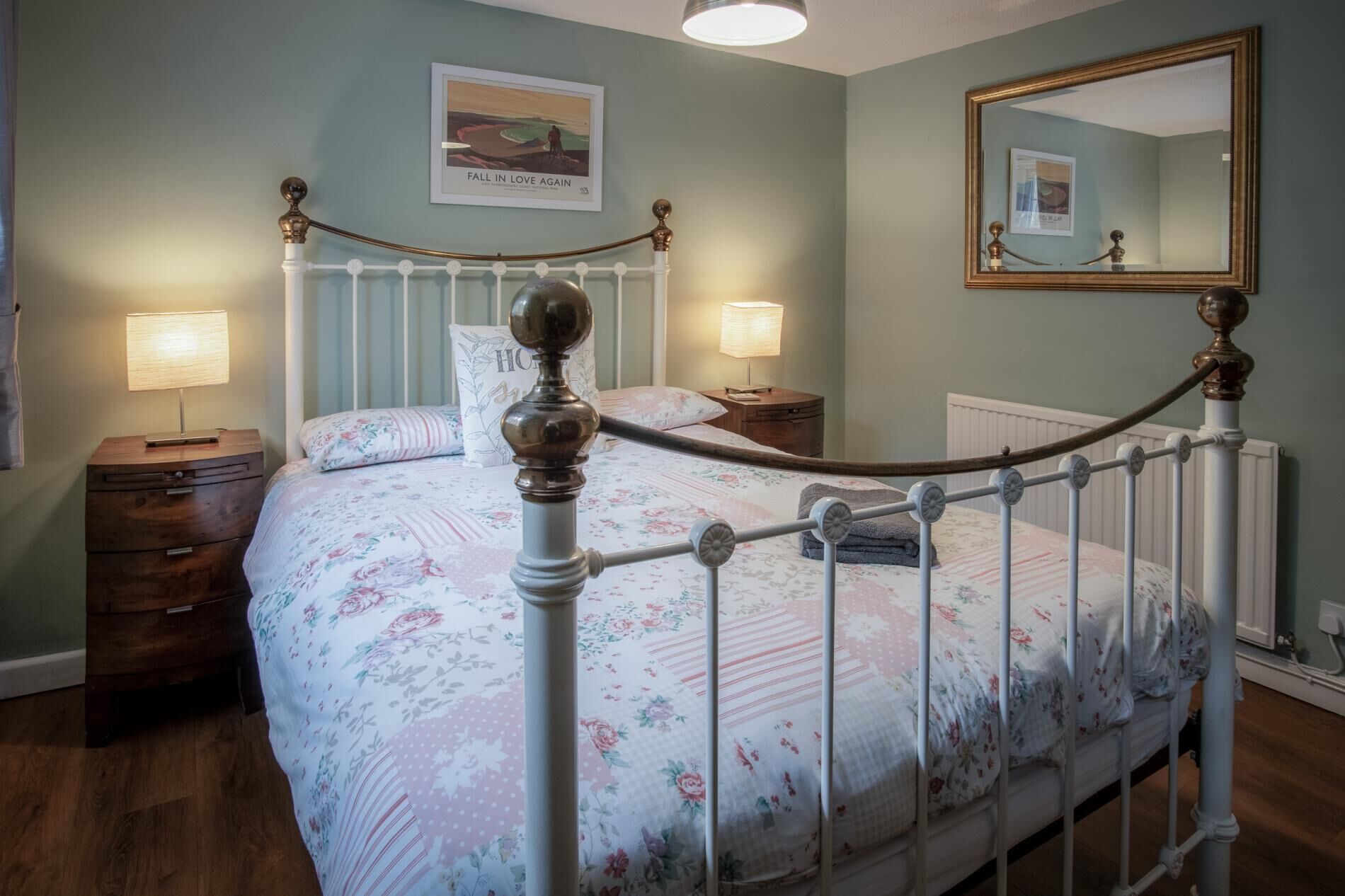A bedroom with a bed, two bedside tables, a dresser, a mirror, and a wall with a poster.