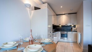 Una cocina moderna con armarios blancos, horno integrado y comedor con una mesa redonda para cuatro.