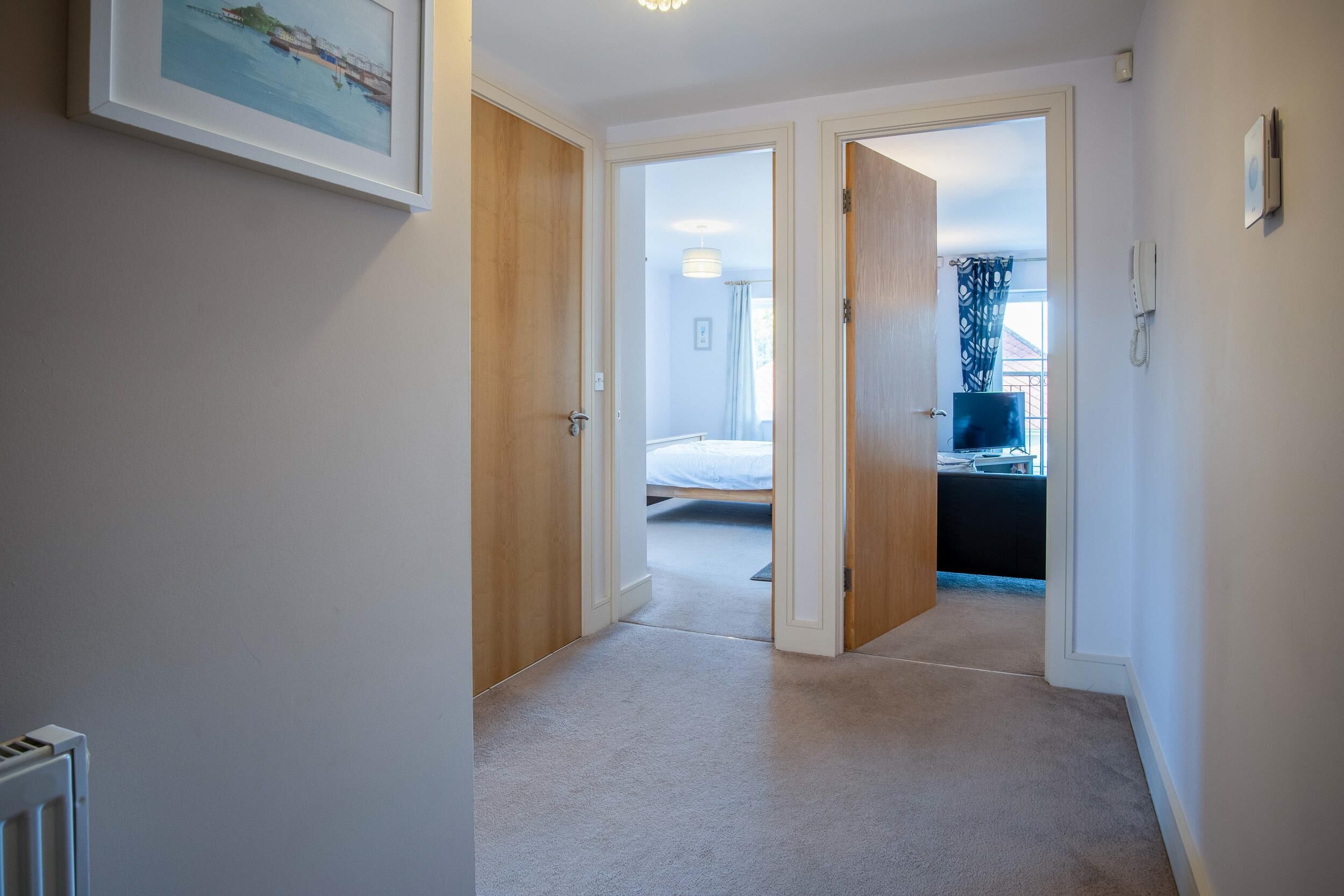 A hallway leading to a bedroom with a bed, a desk, and a chair.