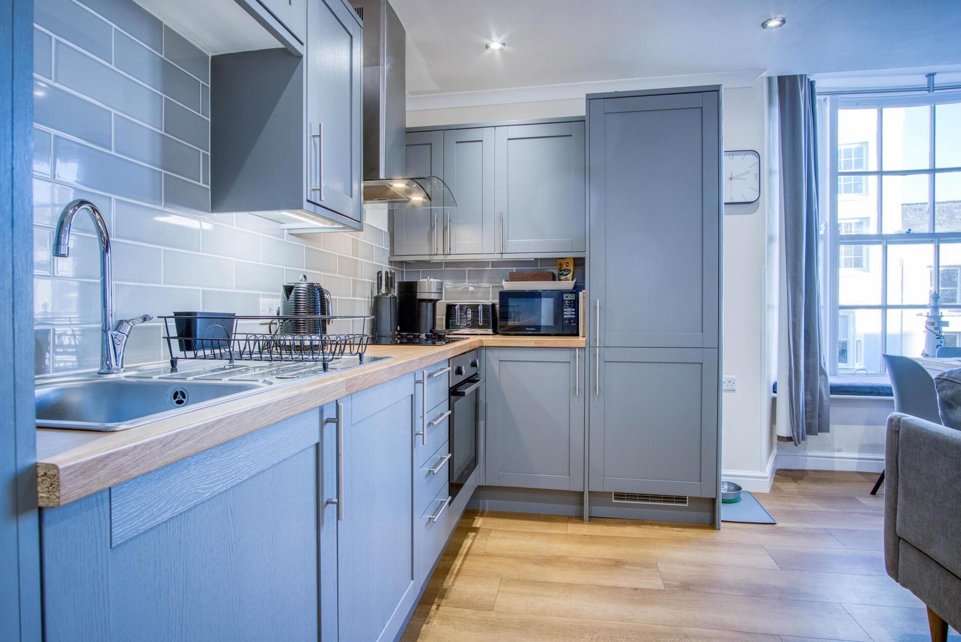 A modern kitchen with grey cabinets, stainless steel appliances, and a wooden countertop.